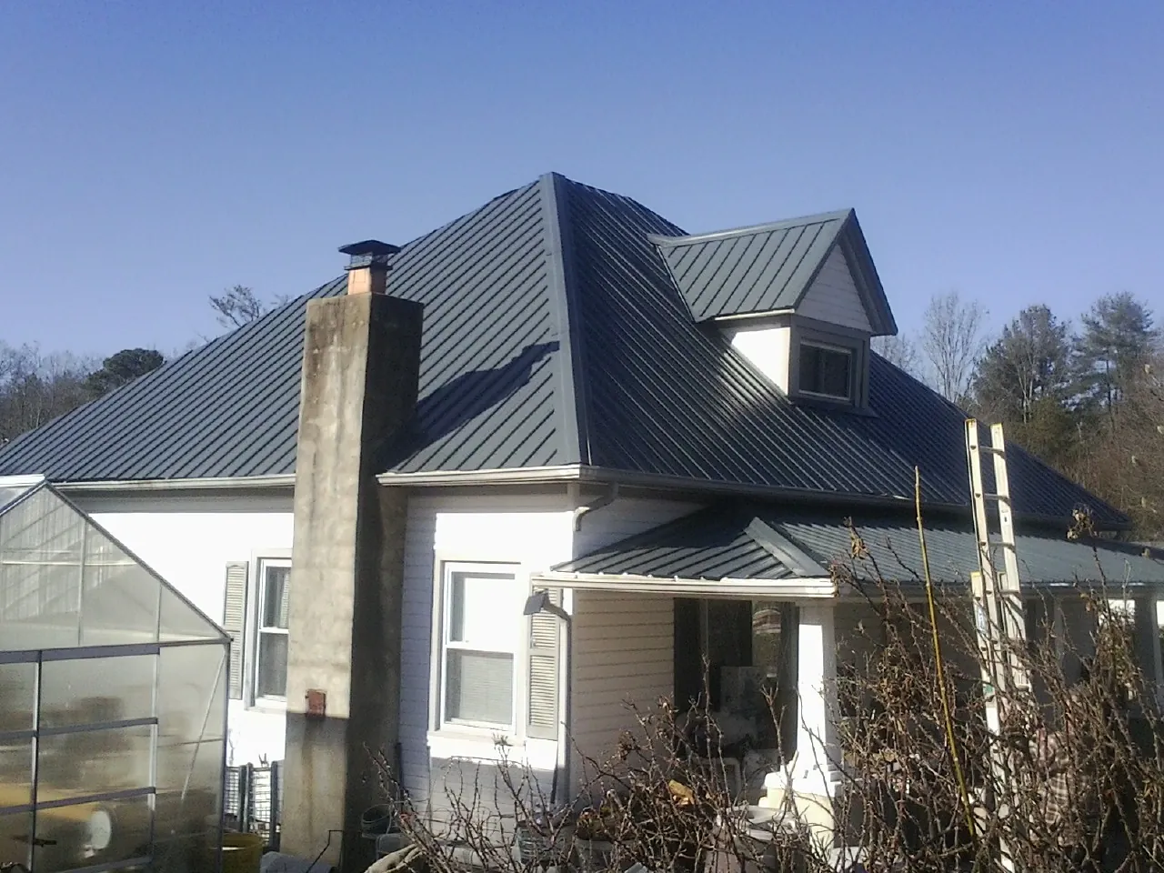 Dark blue standing seam metal roof on a white farmhouse with dormer — Slate & Tile Roof Repair by Roofing Brothers in Bond