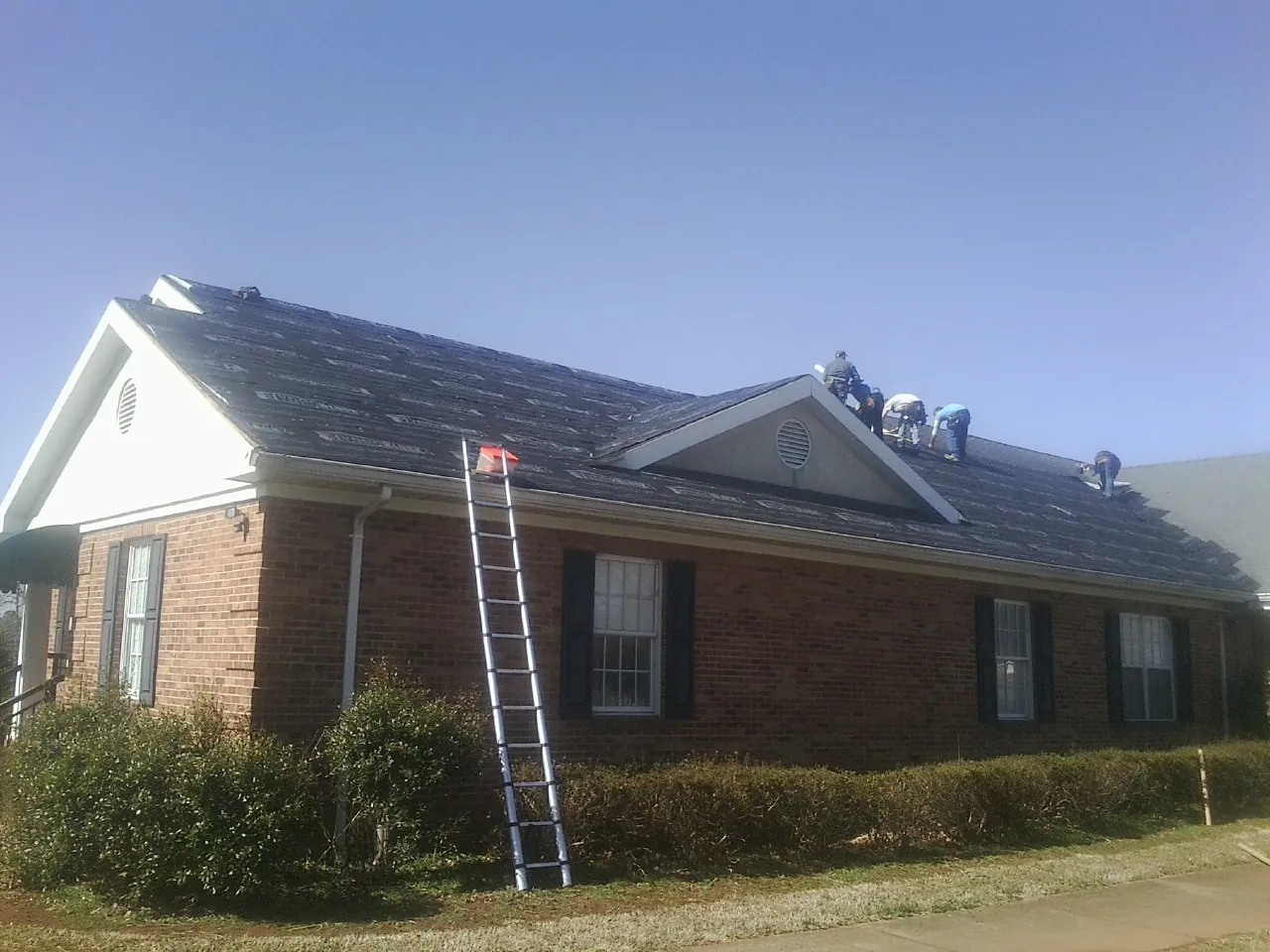 Crew tearing shingles off a brick ranch roof with a ladder set — Emergency Roof Repair work by our crew in Bond