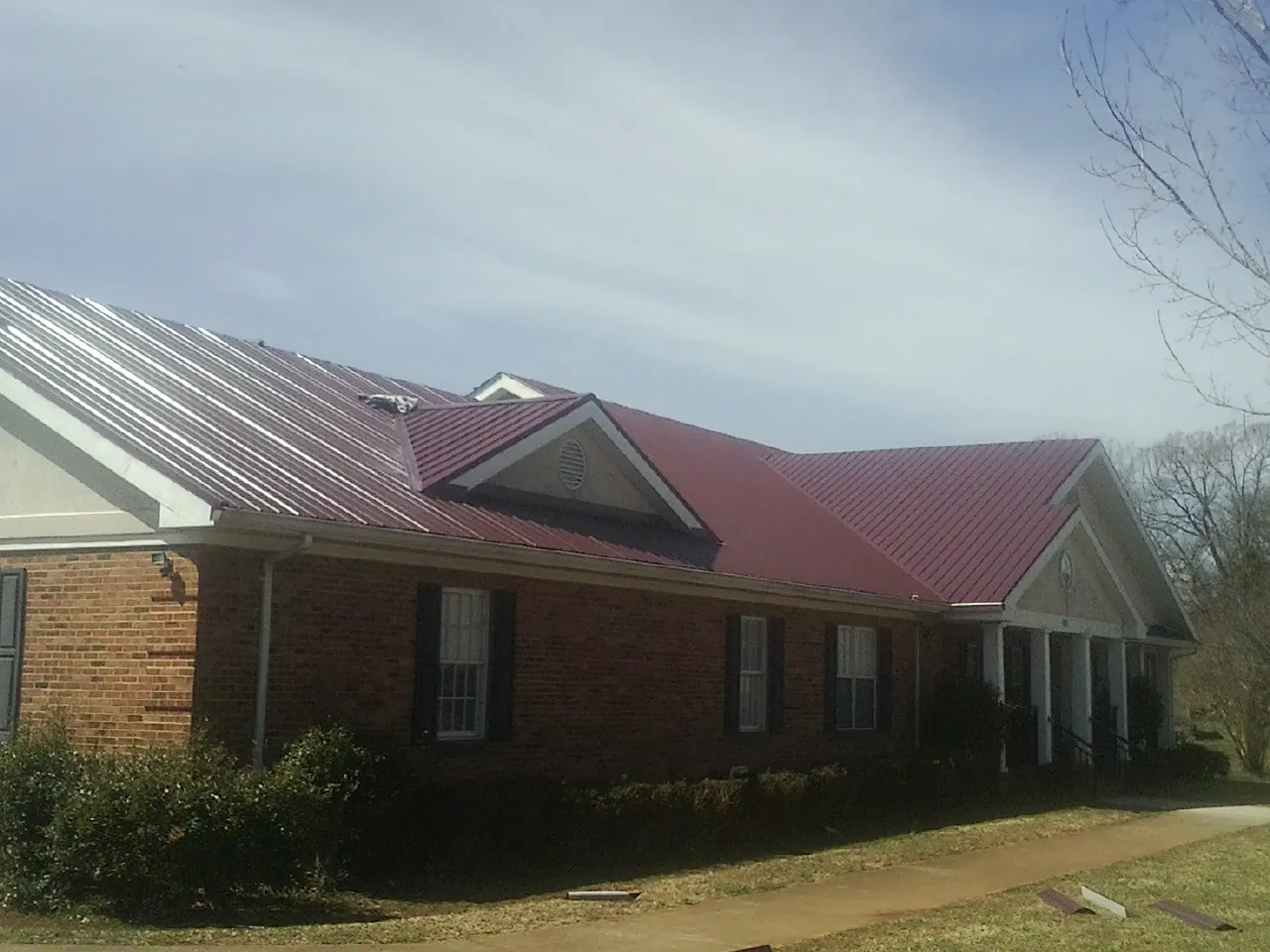 Red metal roof with gabled entries on a long brick building, from a Hail Damage Roof Repair job in Bond