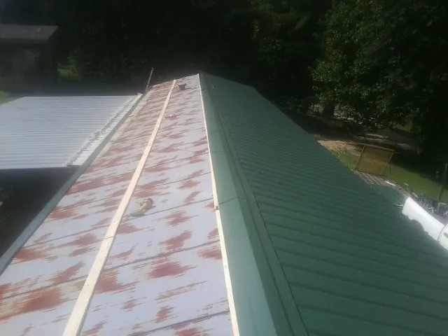 Old rusted panels beside newly installed green metal roofing — Wind Damage Roof Repair by Roofing Brothers in Bond