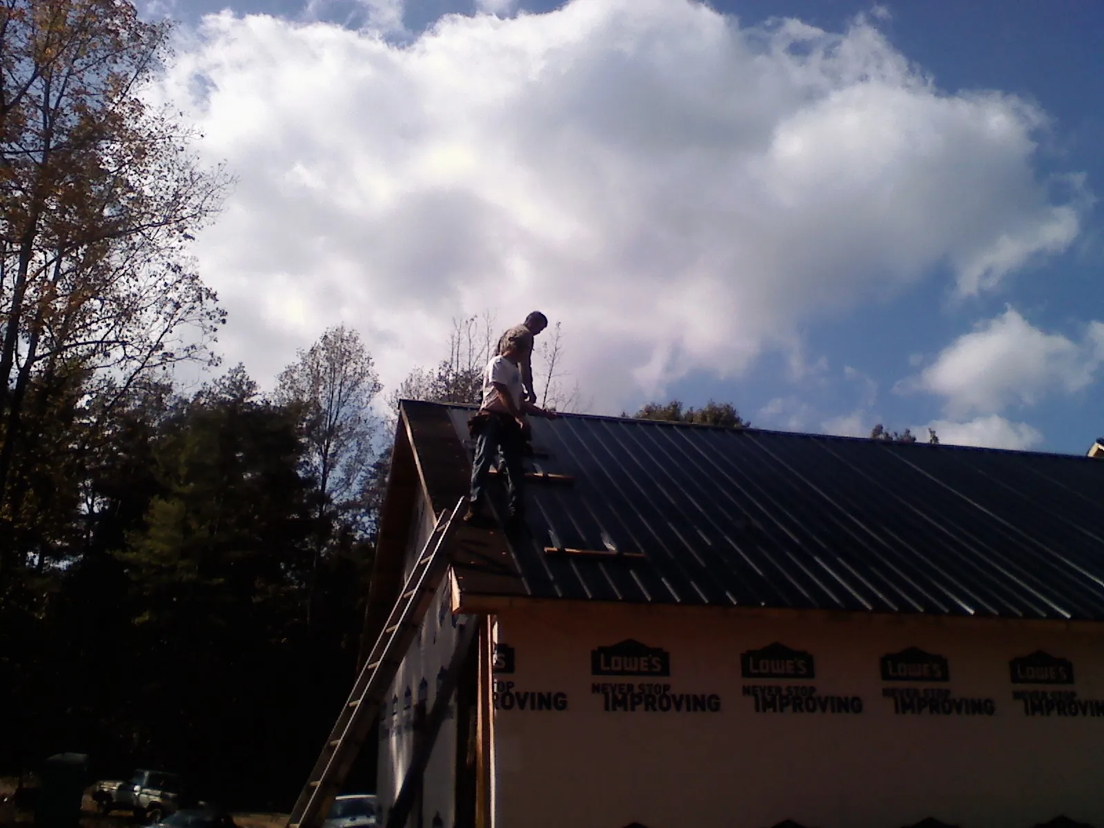 Roofer fastening dark metal panels high against a cloudy sky, from a Roof Inspection job in Bond