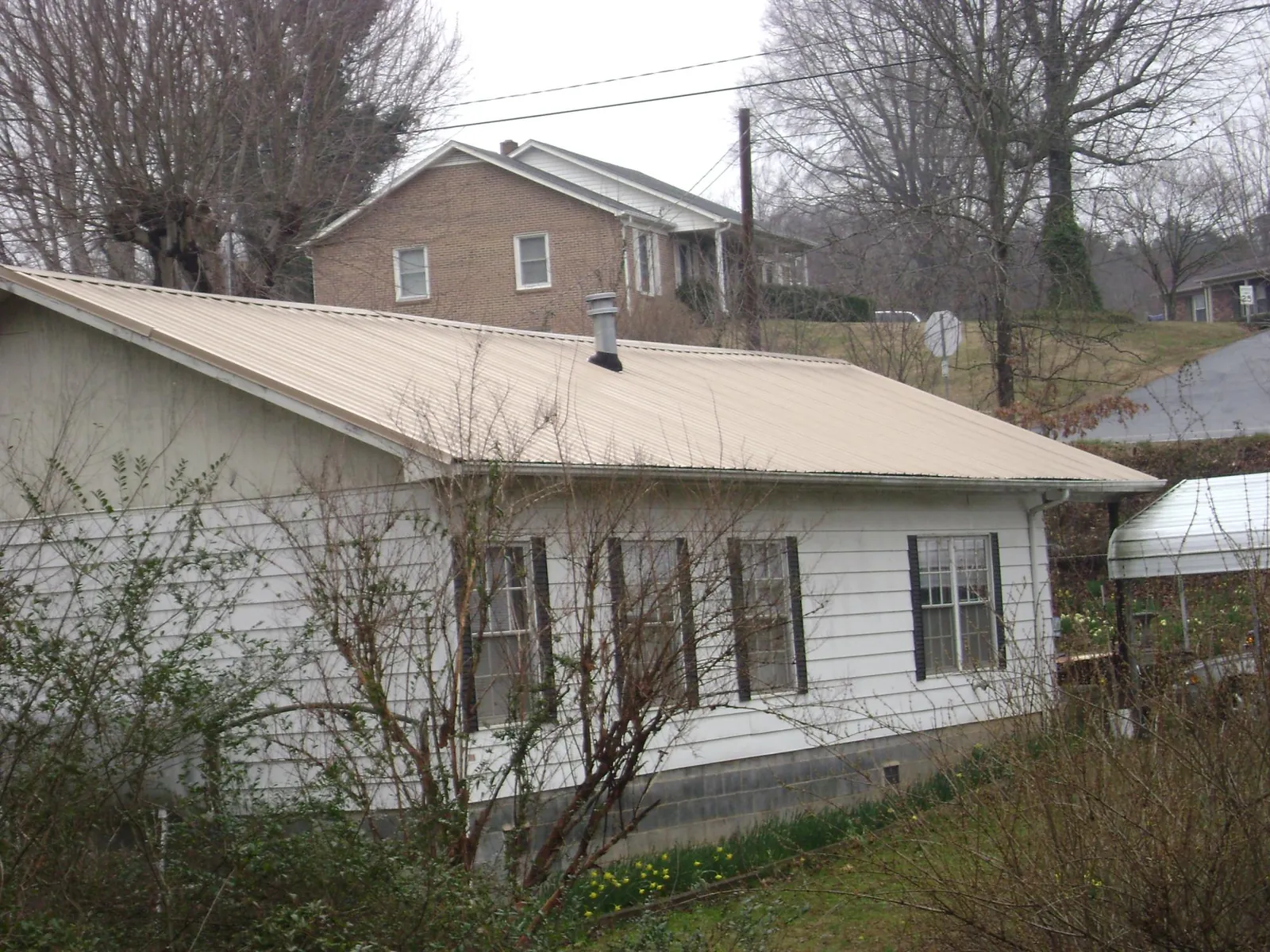 Tan metal roof on a white sided house set into a hillside — Commercial Roofing by Roofing Brothers in Bond