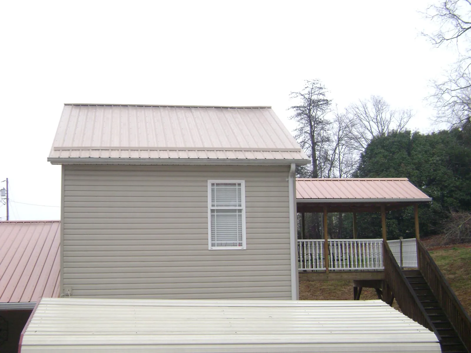 Tan metal roofs on a two story addition and attached porch, from a Roof Replacement job in Bond